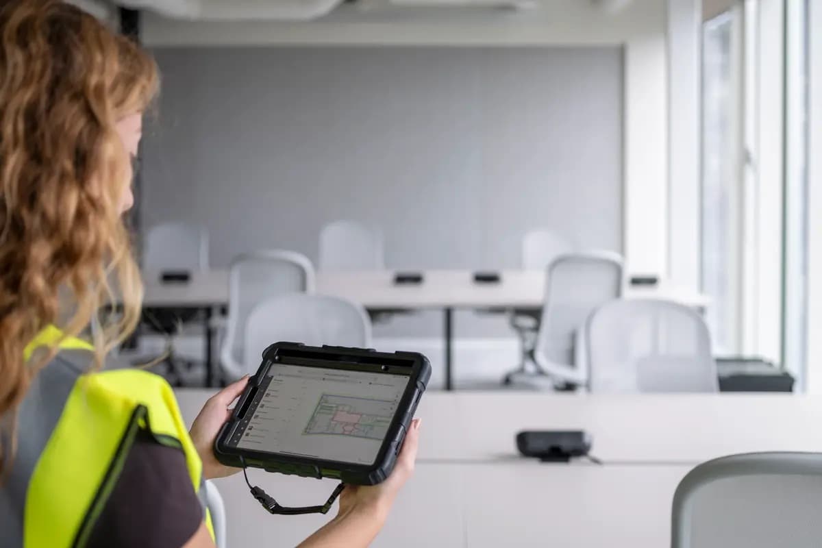 A surveyor holding a rugged tablet in an office being stripped out