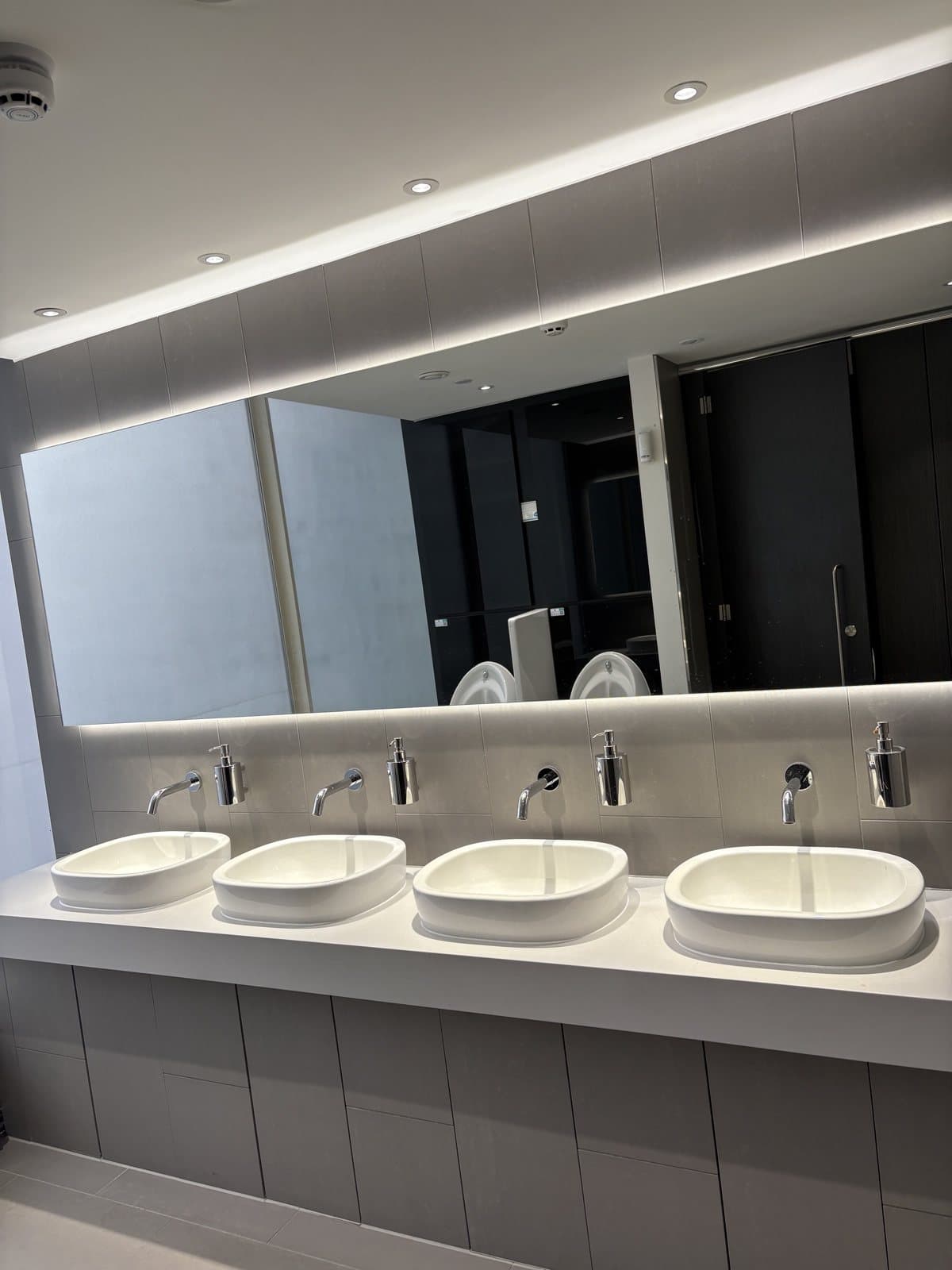 A row of basins and taps in a Peninsular House washroom, brokered for reuse